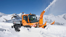 Ein oranger Unimog im Winterdienst räumt die Straße.